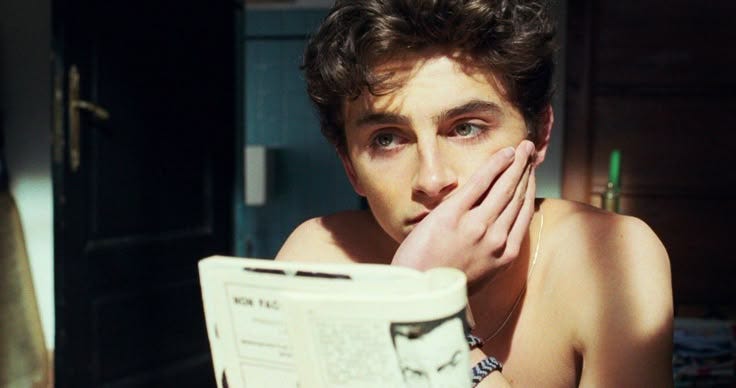 This may contain: a young man reading a newspaper while sitting in front of a mirror with his hands on his face