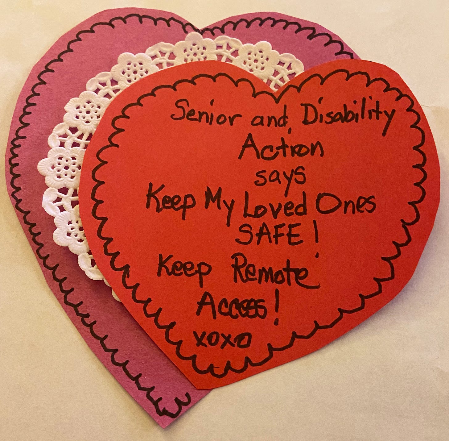 The photo is of a homemade Valentine card, a double construction paper heart sandwiching a doily, decorated with black marker and the words Senior and Disability Action says Keep my loved ones safe! Keep Remote Access! xoxo The photo is of a homemade Valentine card, a double construction paper heart sandwiching a doily, decorated with black marker and the words Senior and Disability Action says Keep my loved ones safe! Keep Remote Access! xoxo