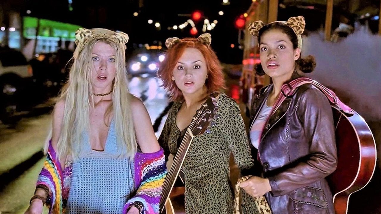 Photo of Josie and the Pussycats standing in the middle of a street with their instruments
