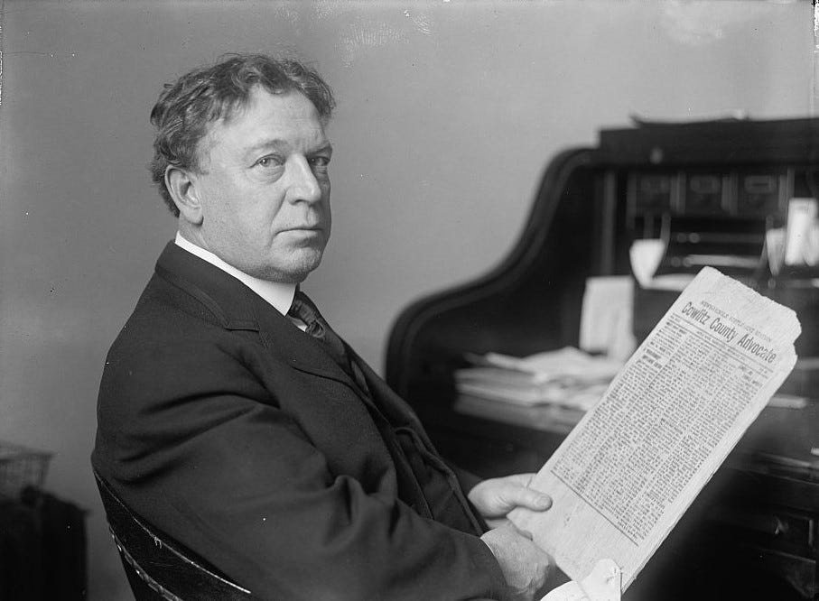 A black and white photo shows a man dressed in a suit holding a newspaper. He sits at a desk and looks sideways to face the camera. A black and white photo shows a man dressed in a suit holding a newspaper. He sits at a desk and looks sideways to face the camera.