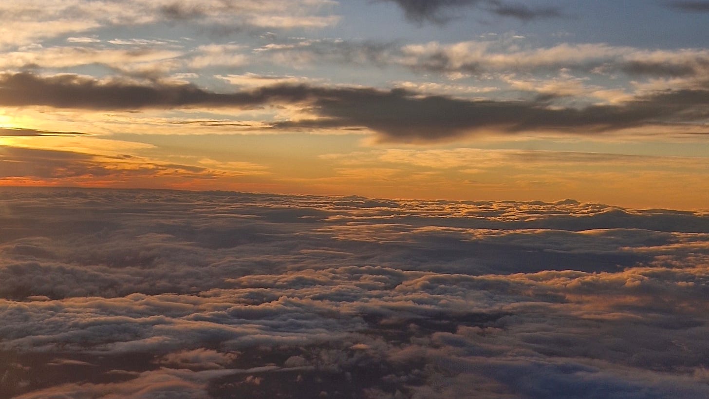 sunset from a plane with clouds and the sky turning orange at the horizon