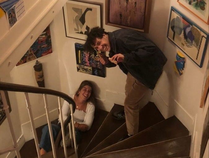 This may contain: two people are standing on the stairs in a room with pictures and paintings above them