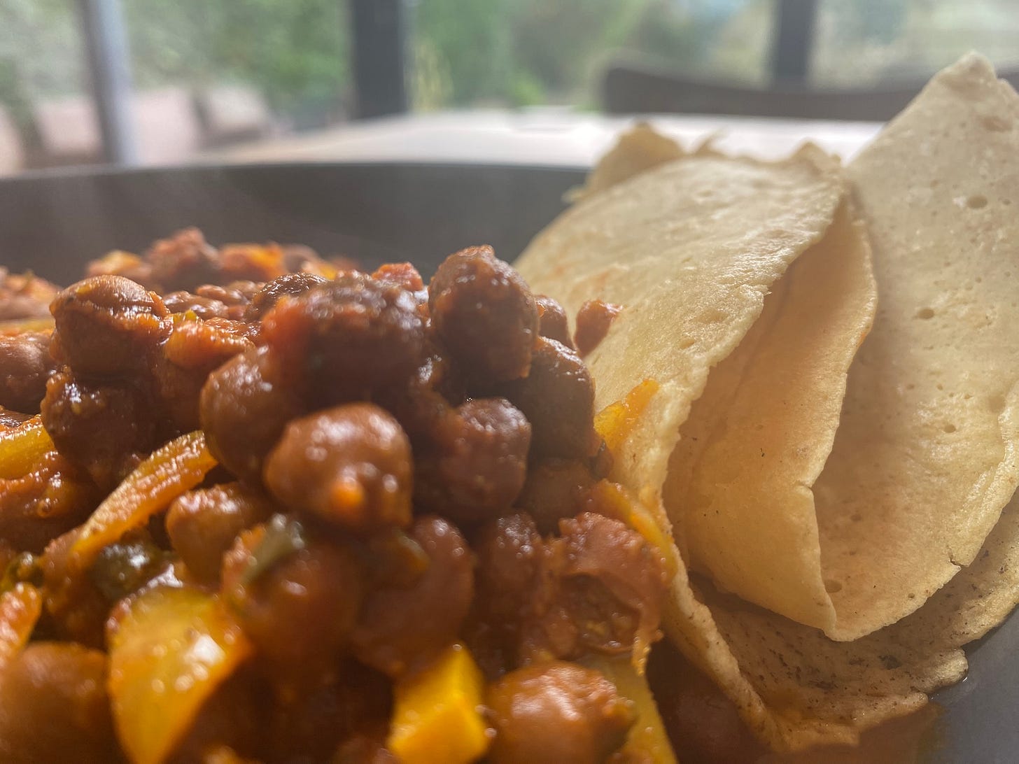 A bowl of chickpeas in a sauce with chopped onions. Next to them is a folded pancake or flatbread.