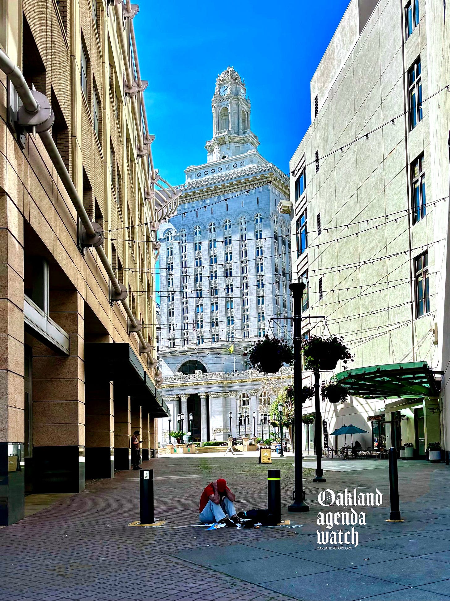 A man sits on the pavement outside Oakland City Hall on Mar. 16, 2026. (Image source: Oakland Report)