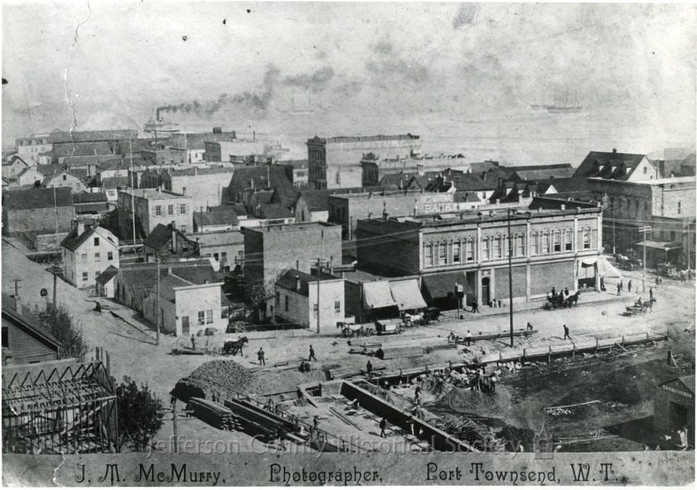 A historic photograph of Port Townsend showing early buildings, streets, and waterfront activity in the late 1800s.