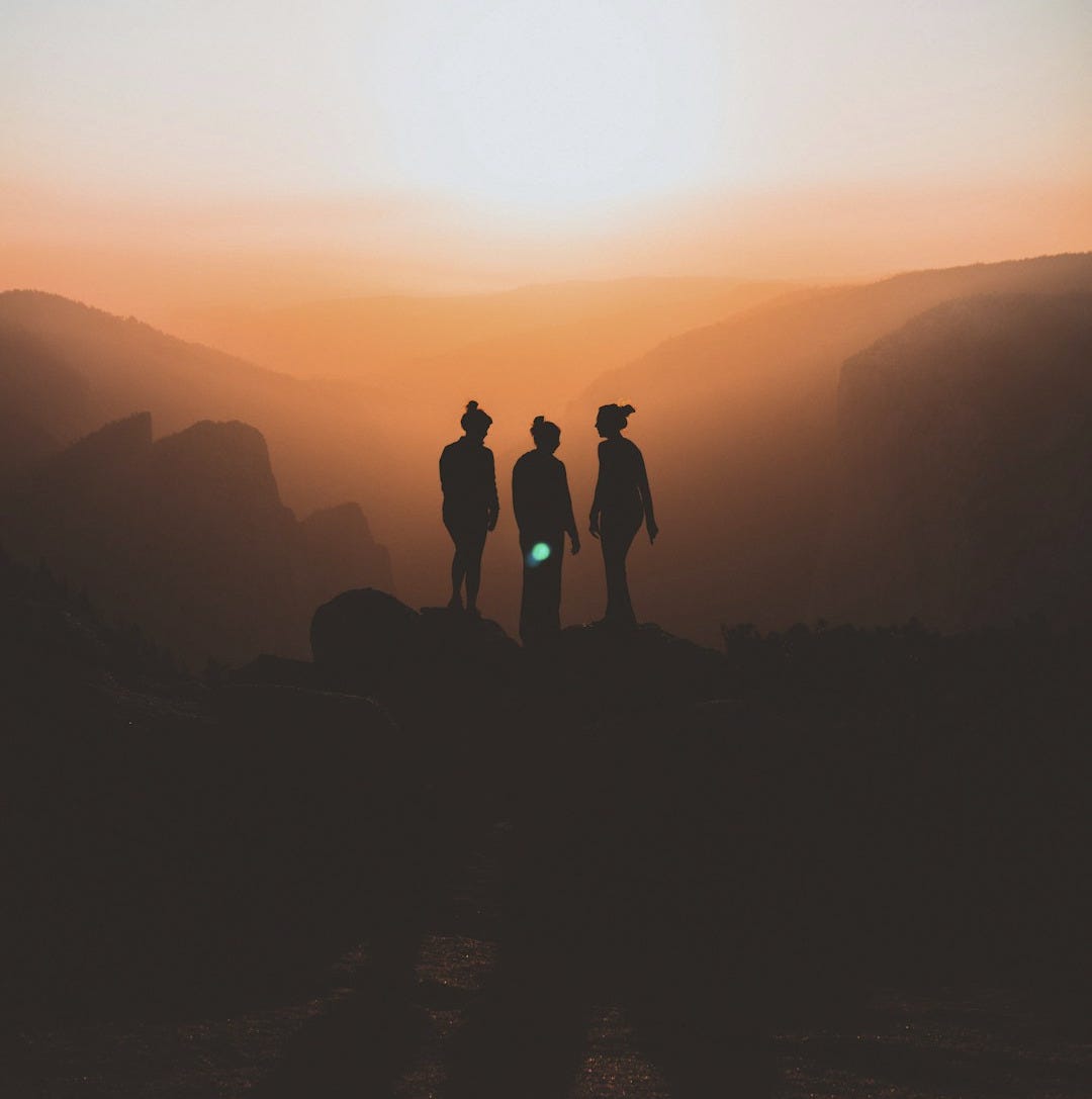 silhouette of three people up on mountain cliff