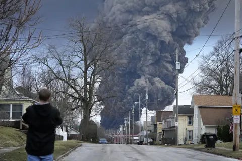 Person on a residential street watching a huge black smoke plume rise over the neighborhood. 