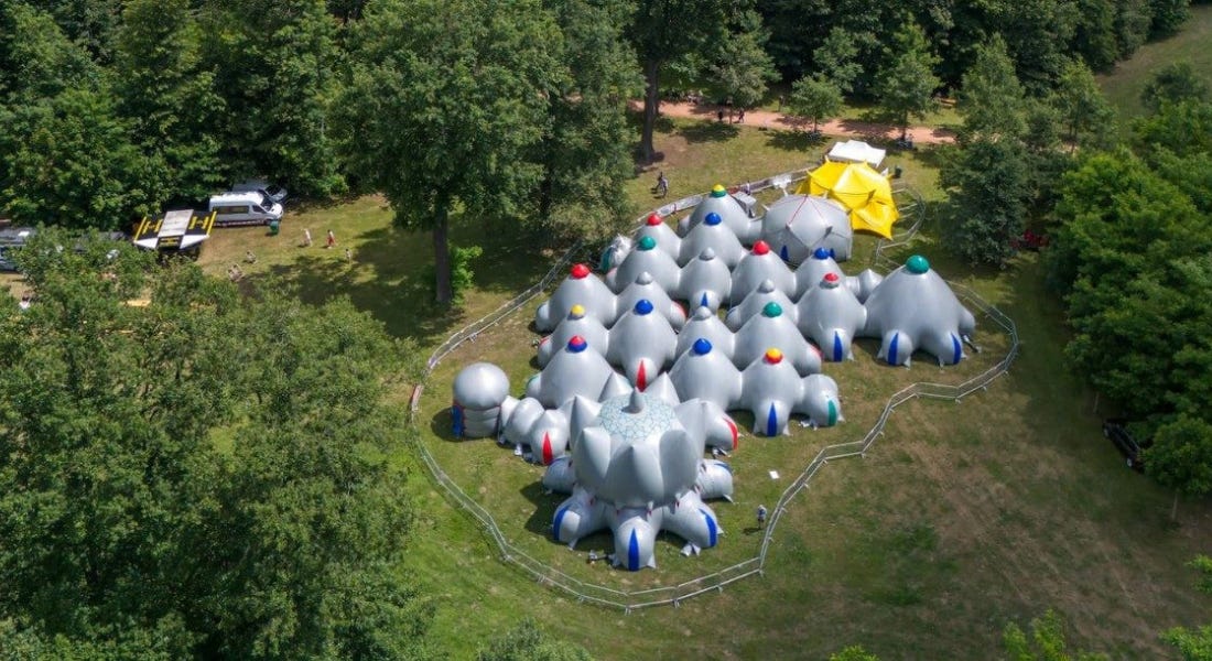 A birds eye view of Luminarium Timisien - a grey inflatable structure with colourful tops, with greenery and trees around it