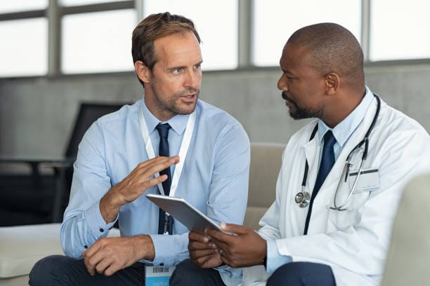 Doctor in conversation with pharmaceutical representative Pharmaceutical representative talking with doctor sitting on couch. African mature practitioner discussing results of the analysis with specialist while consulting diagnosis on digital tablet. Doctor in conversation with medical advisor in hospital room discussing patients report case. pharma companies stock pictures, royalty-free photos & images