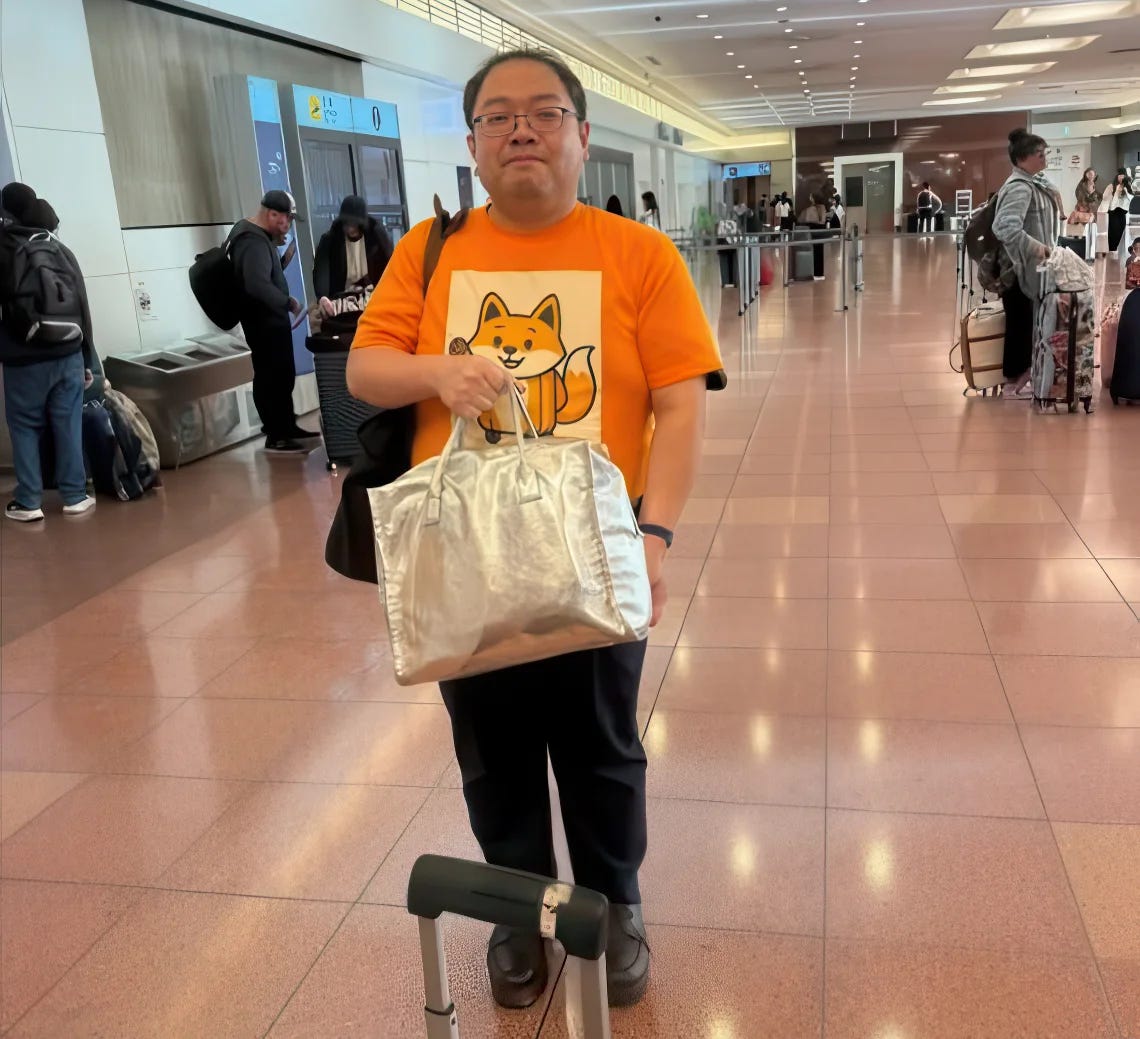 Hitoshi Asami at Tokyo airport arrivals wearing the distinctive orange shirt with fox character, ready to help customers with luggage delivery