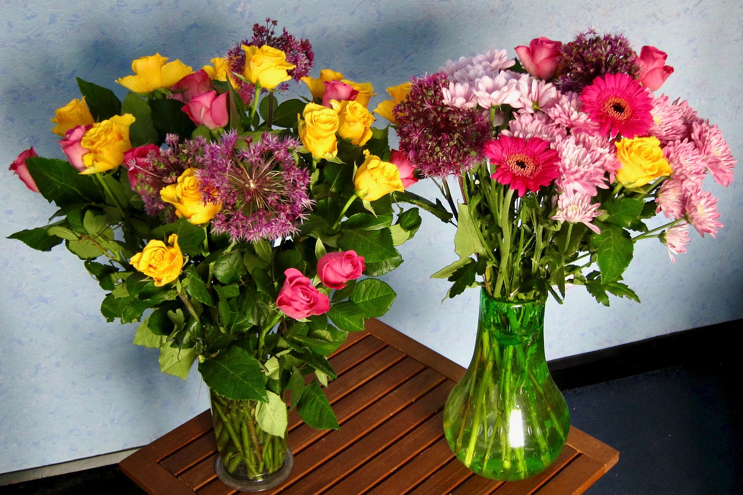 Two vases of colourful flowers on a small wooden table. 