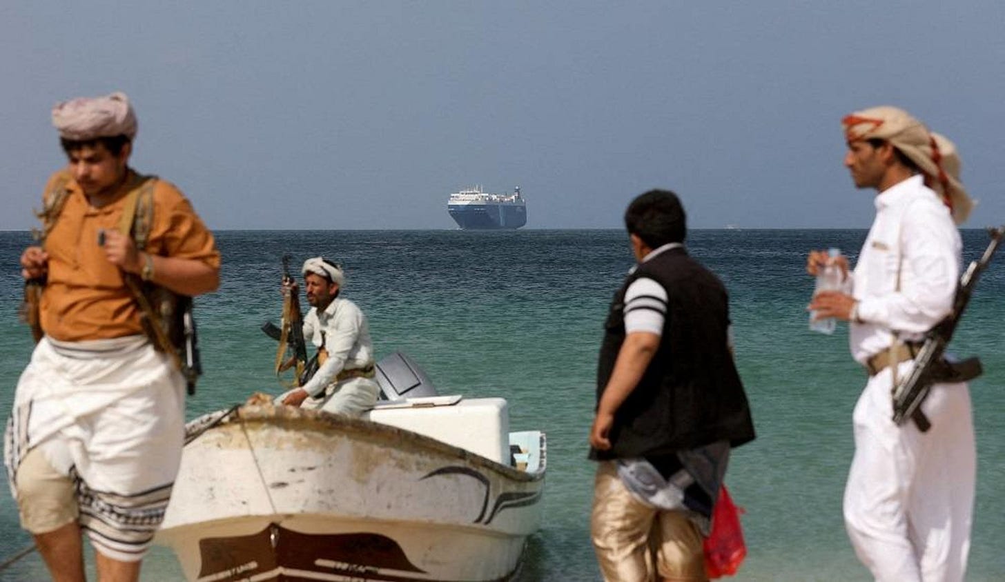 Armed men stand on the beach as the Galaxy Leader commercial ship, seized by Yemen's Houthis last month, is anchored off the coast of al-Salif, Yemen, December 5, 2023. (Reuters) 