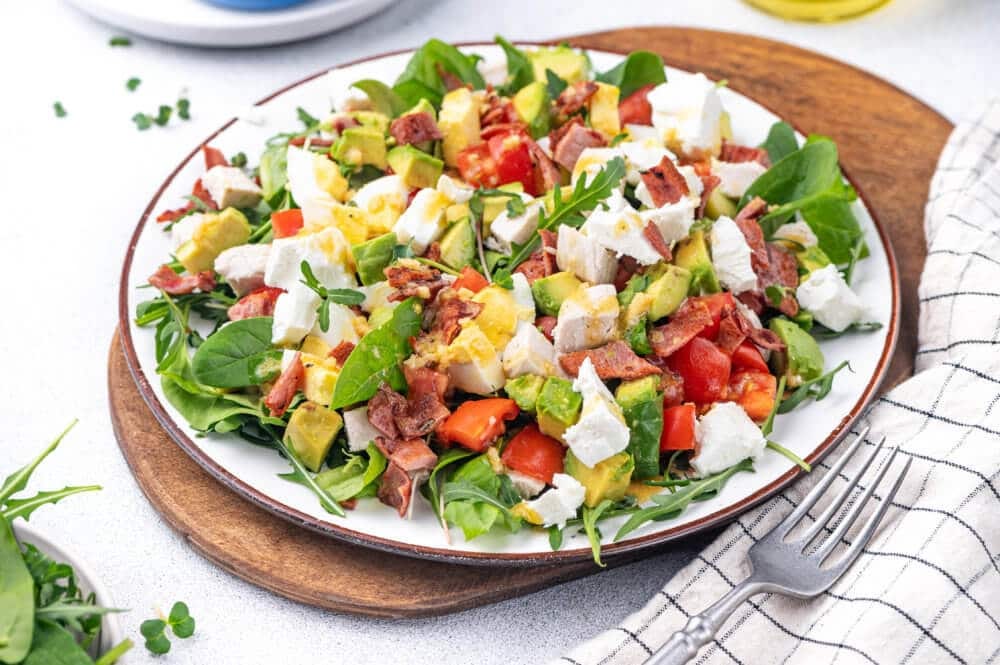chopped lettuce, avocado, tomato, eggs, bacon and chicken on a plate