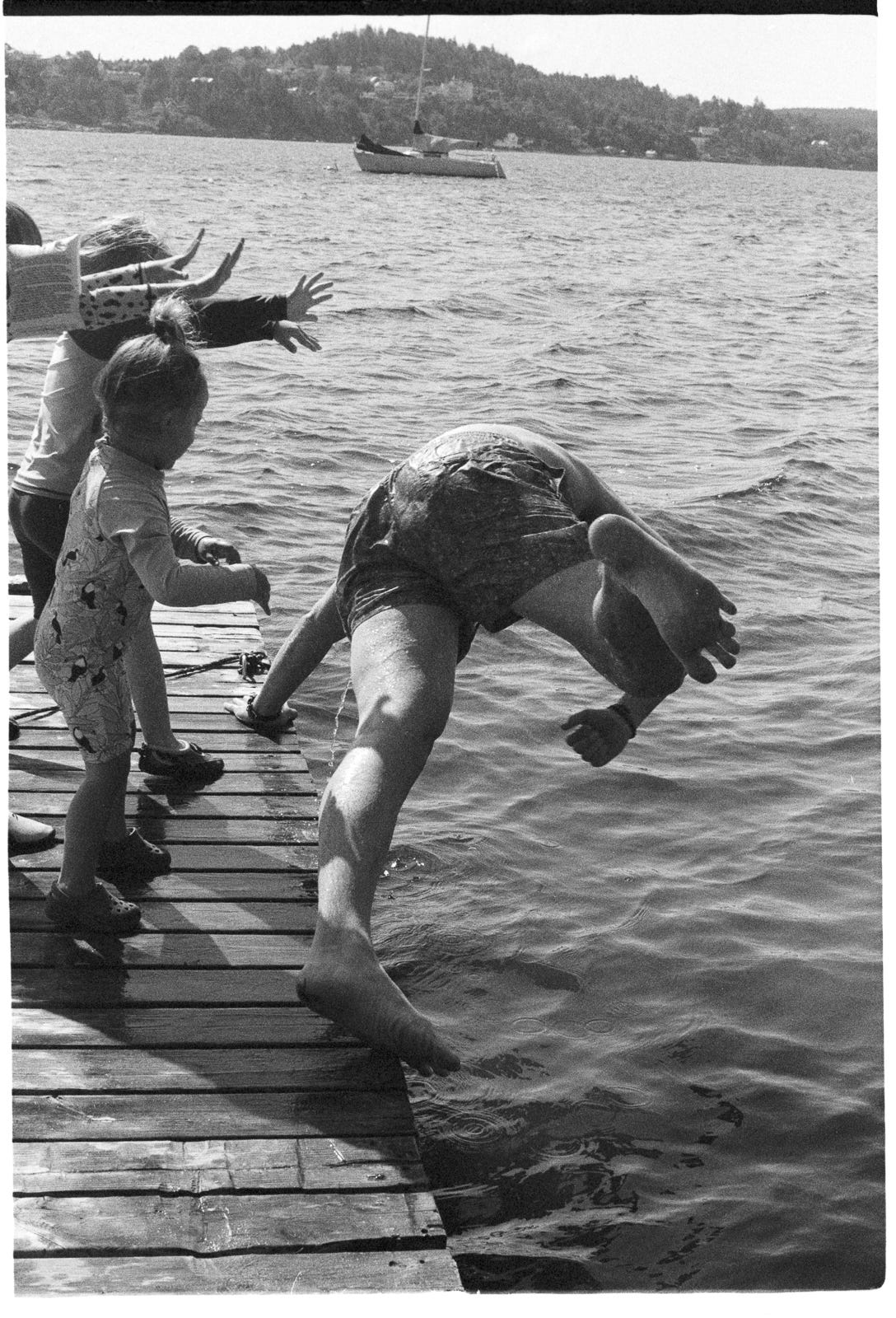 A man is pushed from a floating dock in an ocean bay by a small gang of children. A man is pushed from a floating dock in an ocean bay by a small gang of children.