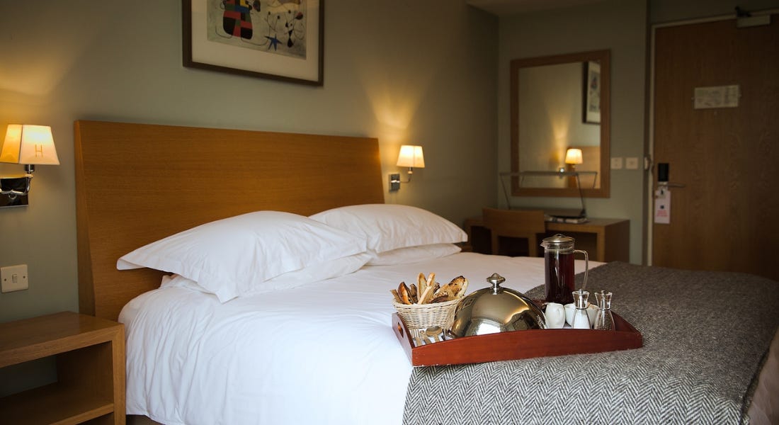 A hotel room with a green wall, wooden headboard, and white bedding