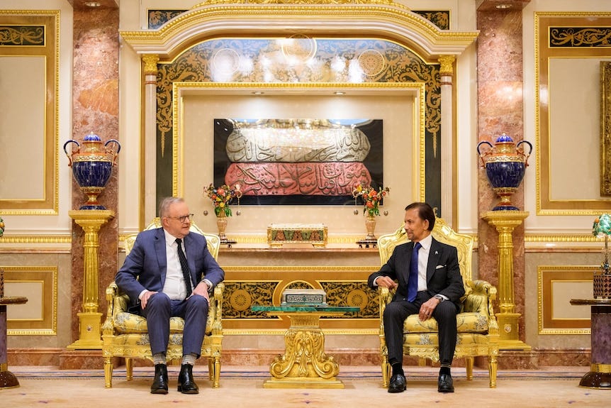 Two men wearing suits sit in gold chairs in a room full of gold and marble decorations. Two men wearing suits sit in gold chairs in a room full of gold and marble decorations.