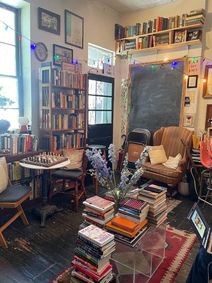 A cozy bookstore filled with shelves and stacks of books and a small bar.