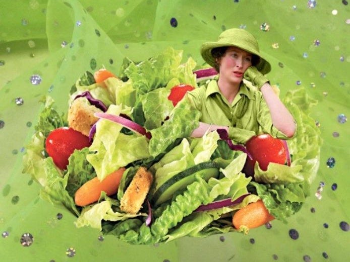 This may contain: a woman sitting on top of a pile of lettuce covered in fruit and vegetables