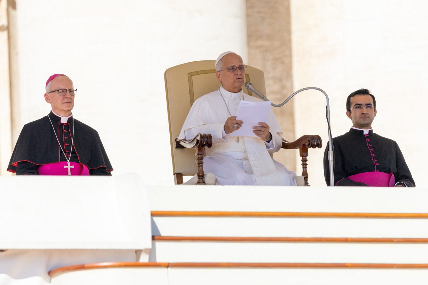 Pope Leo XIV reads his catechesis from a chair in St. Peter’s Square, seated between two aides Pope Leo XIV reads his catechesis from a chair in St. Peter’s Square, seated between two aides