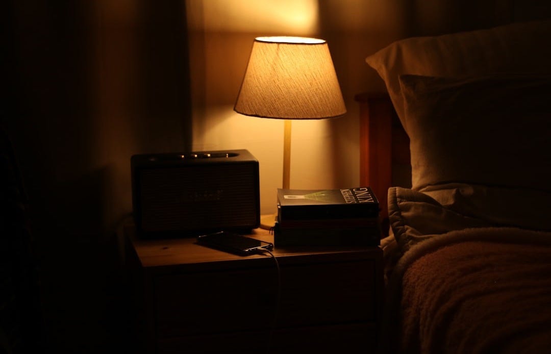 A bedside lamp illuminates a nightstand with a radio.