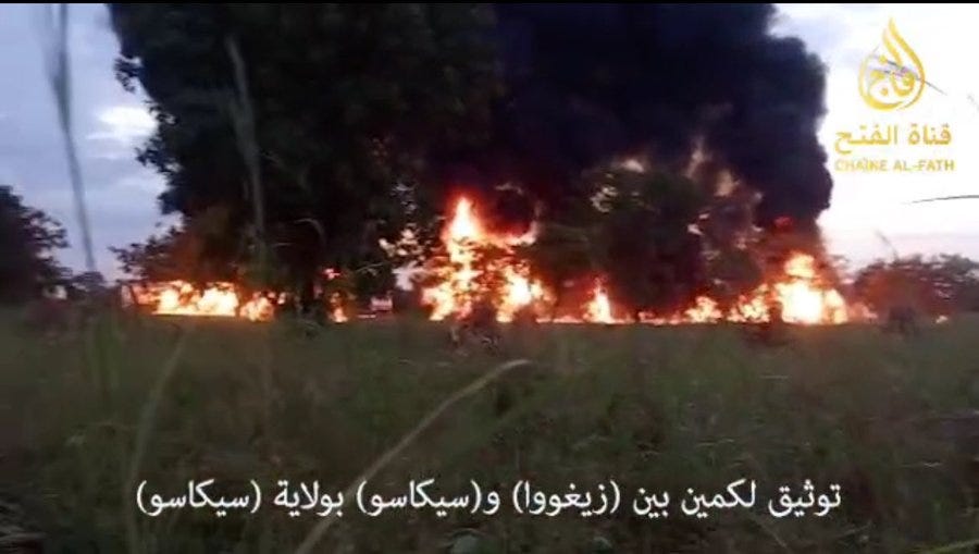 Grassy field at twilight with multiple tanker trucks engulfed in flames and thick black smoke rising, surrounded by trees, Arabic text overlay at bottom reading attack details in Sikasso region, Al-Fatah Media logo in top right corner. Grassy field at twilight with multiple tanker trucks engulfed in flames and thick black smoke rising, surrounded by trees, Arabic text overlay at bottom reading attack details in Sikasso region, Al-Fatah Media logo in top right corner.