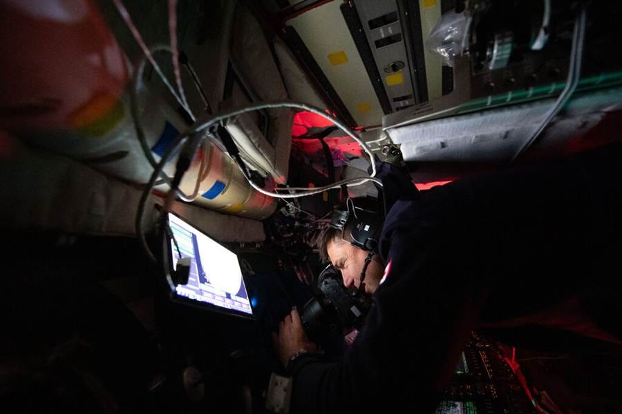 An astronaut peers through a lens that is focused on the moon from inside a spacecraft. An astronaut peers through a lens that is focused on the moon from inside a spacecraft.