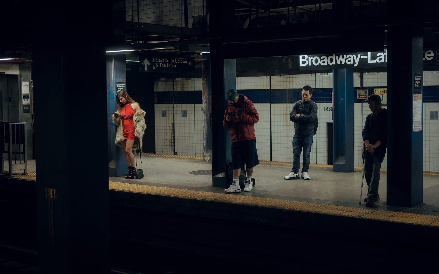 A subway platform populated by four commuters, one of whom is a woman wearing a bright red dress and pumps.