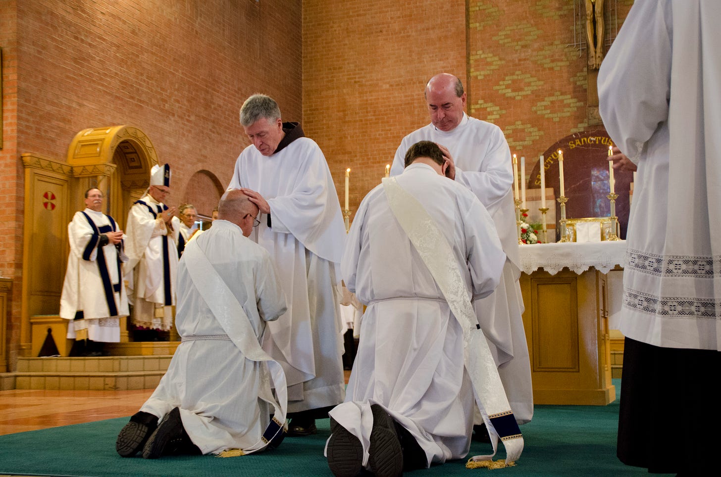 Frs. Dale Jamison (standing, left) and Jay Jung (standing, right) lay hands on the heads of new priests David Tate (kneeling, left) and Joshua Mayer (kneeling, right)