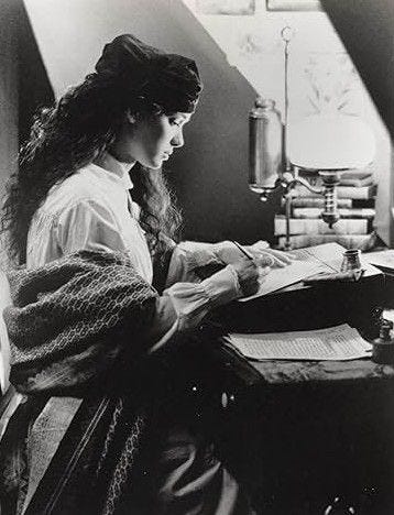 This may contain: an old photo of a woman sitting at a desk