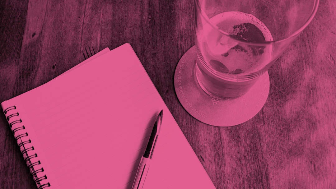 A notebook and pen next to a pint of beer.