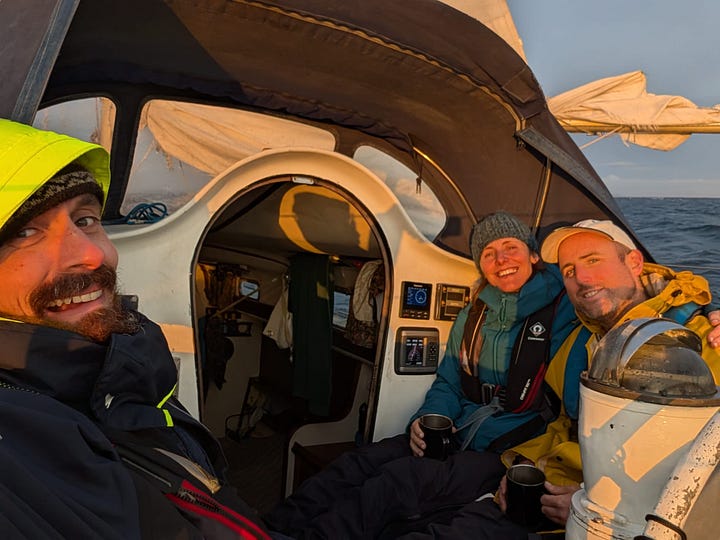 Three people on a boat drinking tea, looking a bit seasick and cold