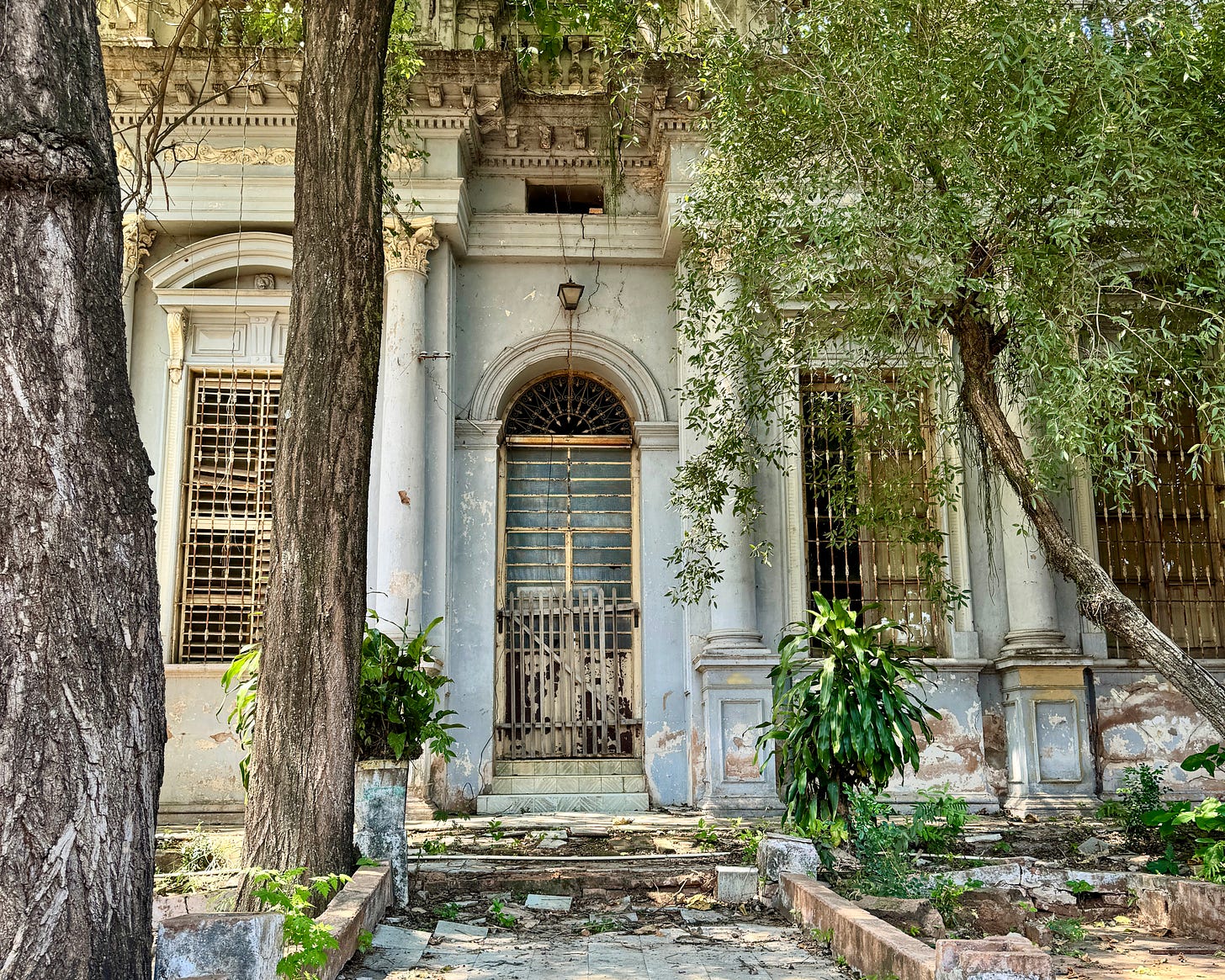 Edificio histórico estilo ecléctico destartalado en Asunción con árboles y vegetación delante. 