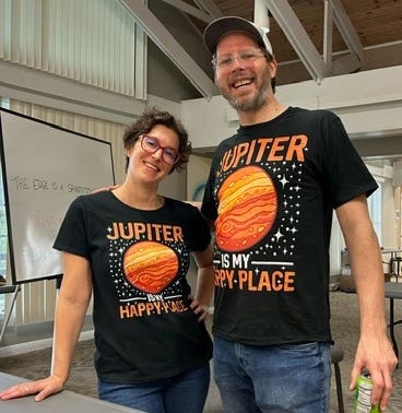 short white woman and tall white man in black t-shirts that read Jupiter is My Happy Place