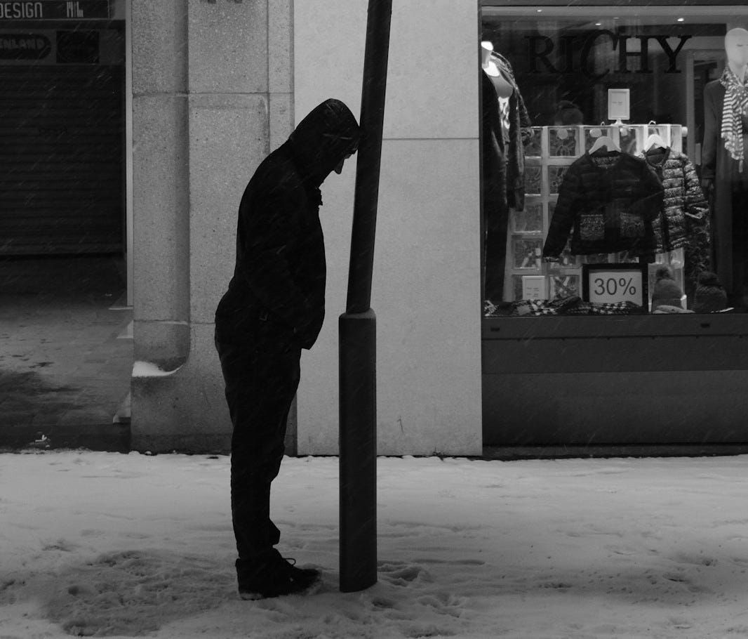 grayscale photo of man in black hoodie standing near glass window grayscale photo of man in black hoodie standing near glass window