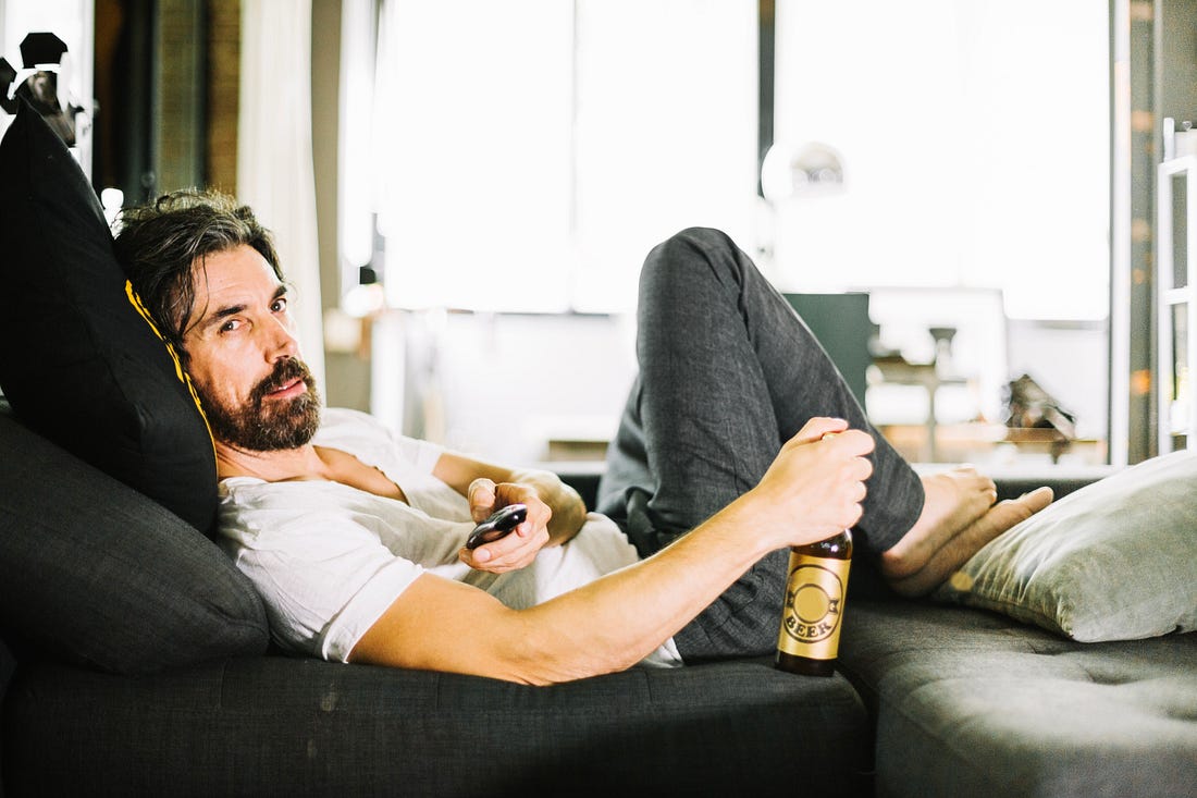 man lounging on couch with beer and tv remote