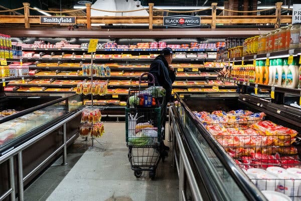 A man with a shopping cart looks at products in a grocery store.