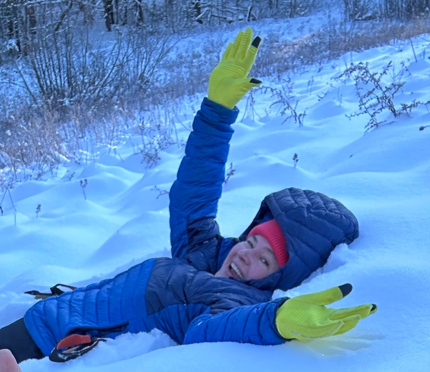 A photo shows guest post author, Emilie, lying on her back in the snow. Smiling big, she wears a large blue winter coat and yellow gloves.