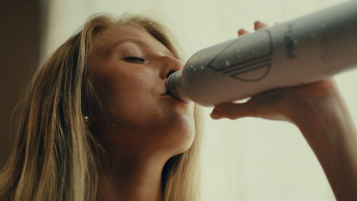 A photo of a blonde woman drinking out of a metal water bottle.