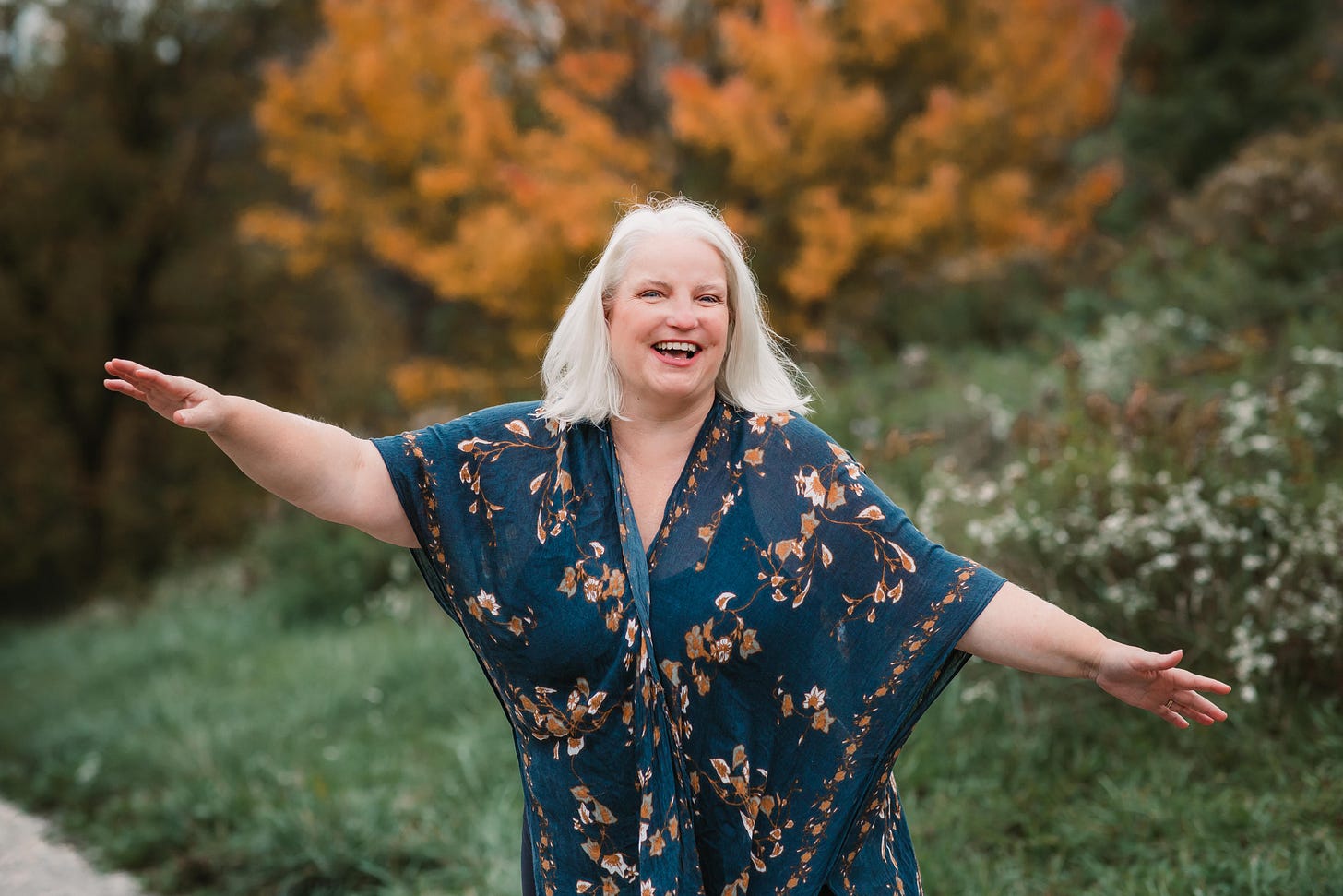a woman with white shoulder length hair laughing with her arms extended to the side.