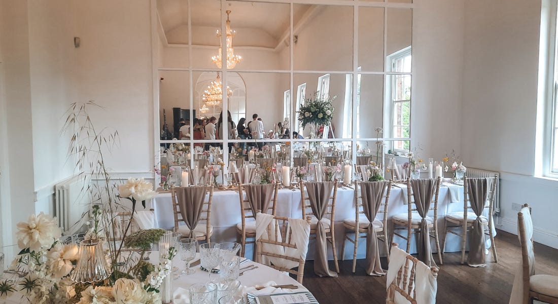 A white dining area with white tables, a large window, and chandeliers A white dining area with white tables, a large window, and chandeliers