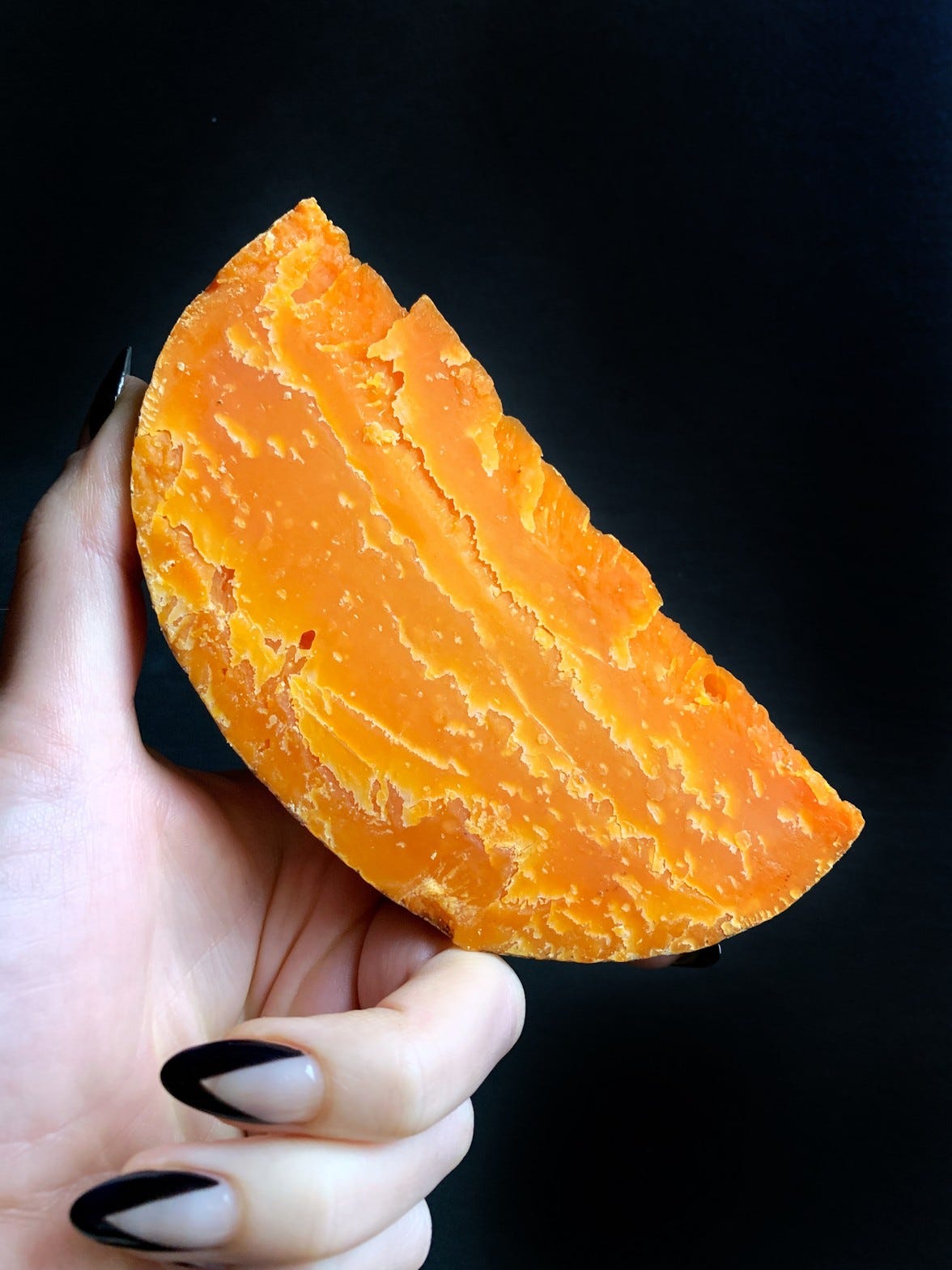 Hand holding an extra aged wedge of Mimolette