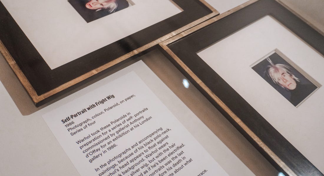 Two framed polaroid photographs of Andy Warhol next to a label Two framed polaroid photographs of Andy Warhol next to a label