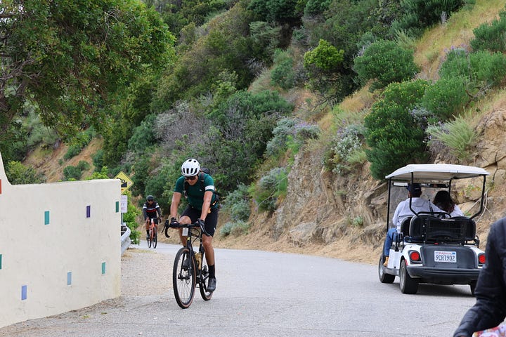 Cyclists climbing up a steep road and reaching a vista point at the top of the climb