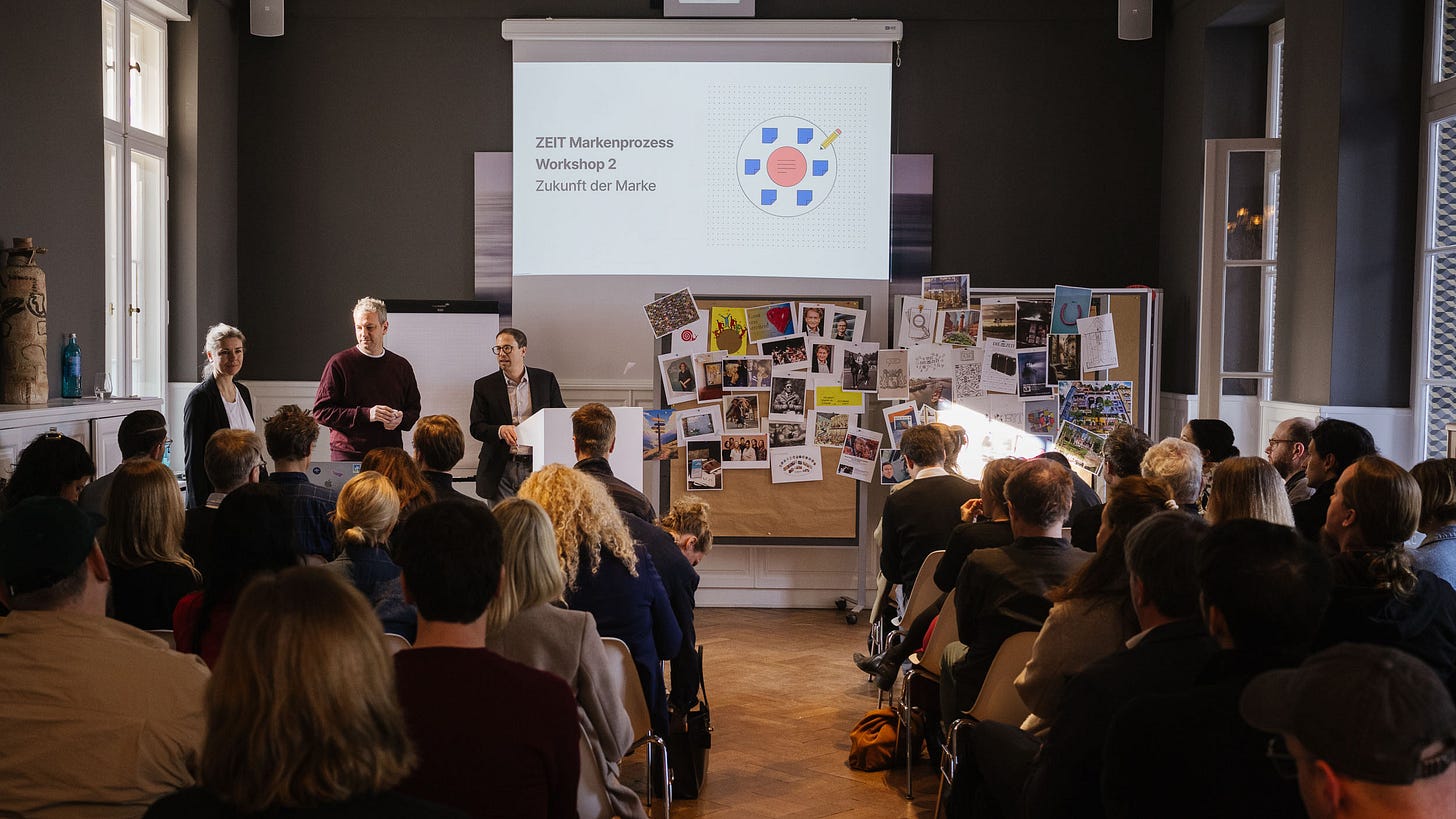 Workshop-Präsentation des ZEIT Markenprozesses – Workshop 2 „Zukunft der Marke" mit Publikum, drei Moderierenden vor einer Leinwand und einem mit Fotos bestückten Pinnwand-Display in einem hellen Veranstaltungsraum Workshop-Präsentation des ZEIT Markenprozesses – Workshop 2 „Zukunft der Marke" mit Publikum, drei Moderierenden vor einer Leinwand und einem mit Fotos bestückten Pinnwand-Display in einem hellen Veranstaltungsraum