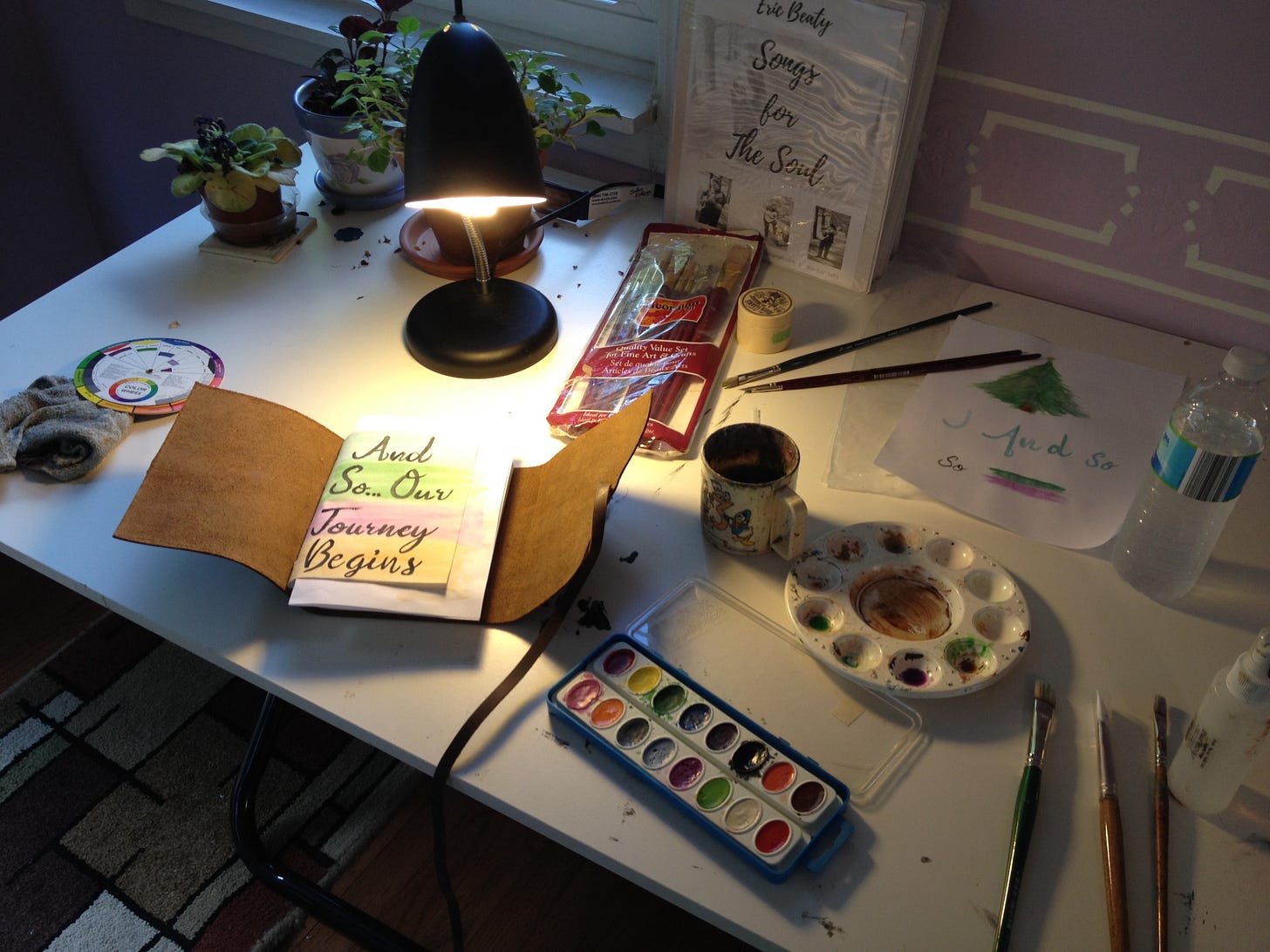 handmade leather journal with caligraphy handwriting written on the first page laying open on an art desk with art supplies