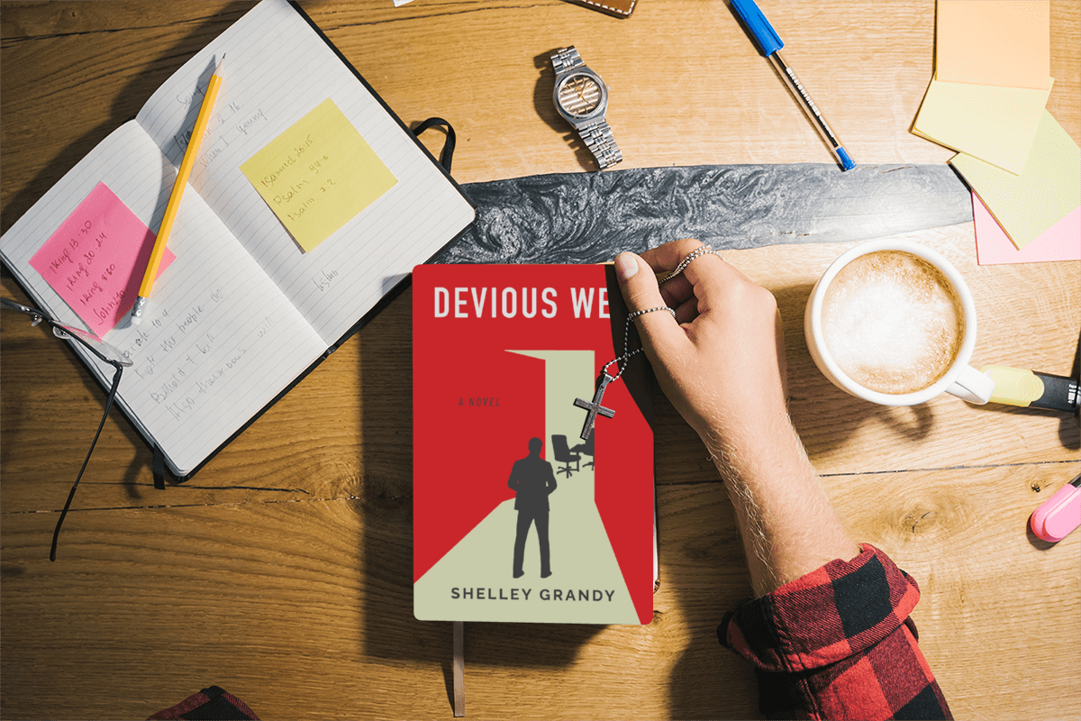 Book "Devious Web" on desk next to notebook and a woman's arm