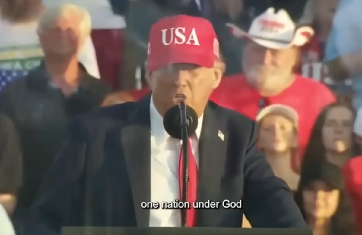 Trump wearing a red USA hat and speaking to supporters; subtitle says «one nation under God»