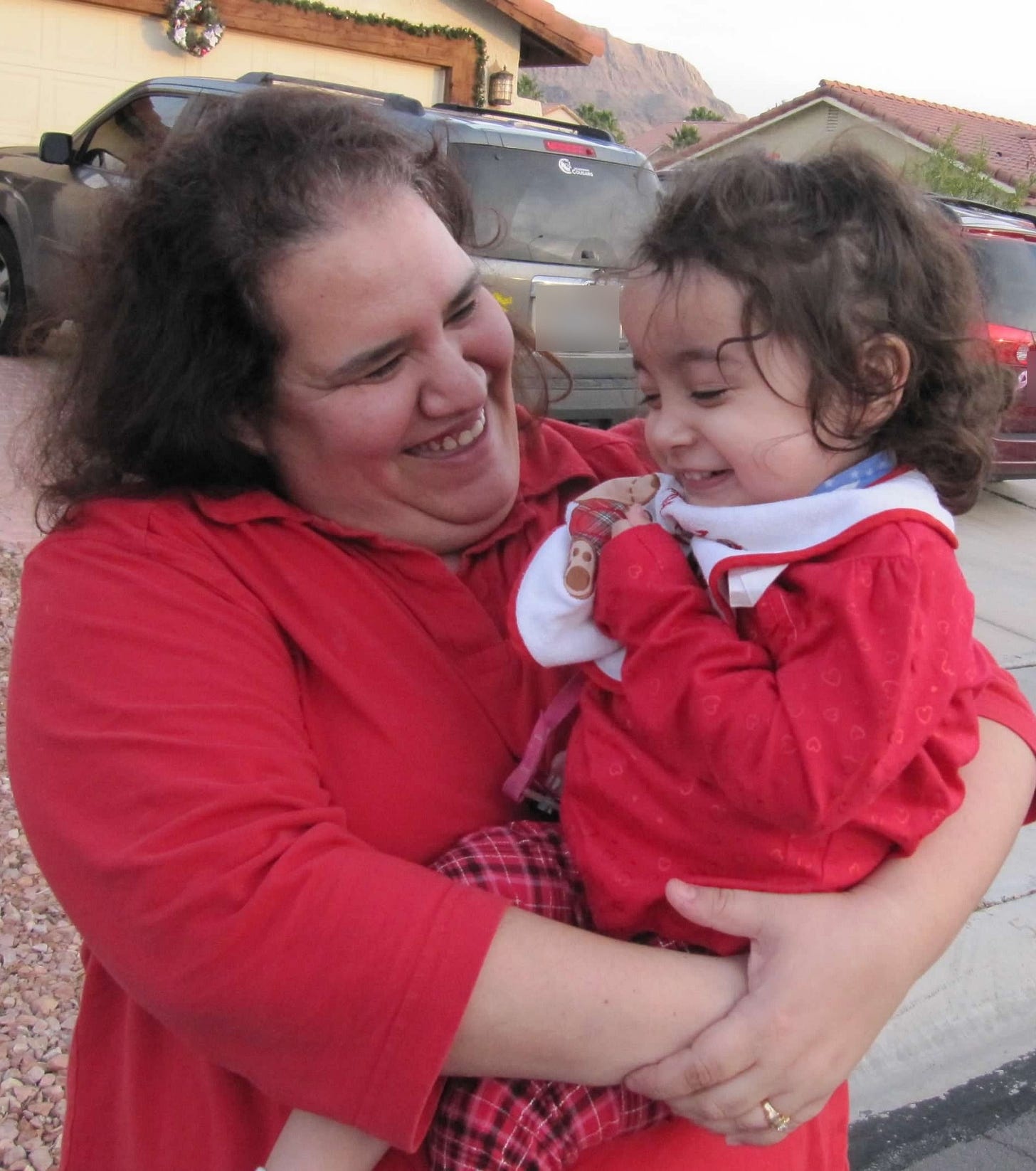 Carrie smiling and holding her young daughter Hannah, who is laughing. Both are wearing red. Carrie smiling and holding her young daughter Hannah, who is laughing. Both are wearing red.