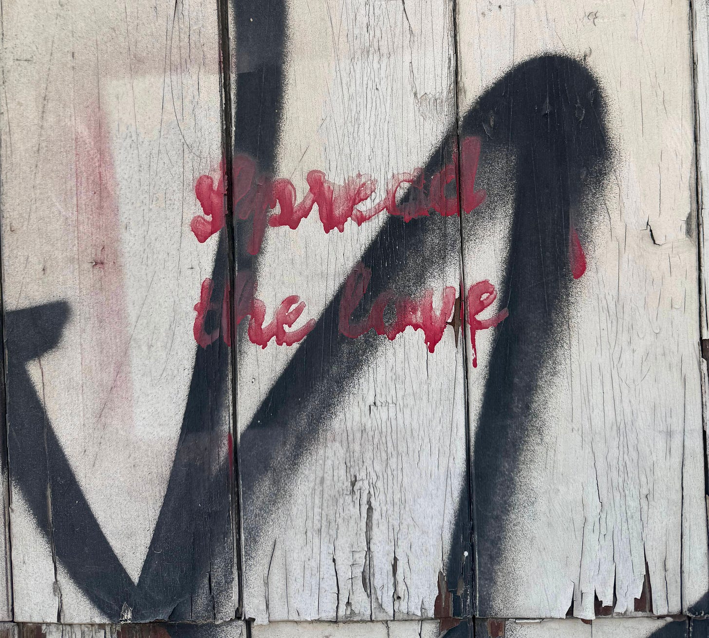 Close-up of weathered white painted wood boards with peeling paint, overlaid with black spray paint marks and red cursive text reading "spread the love."