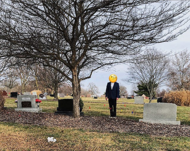 Man standing near a tree and between two headstones in a cemetery on a cold winter day 
